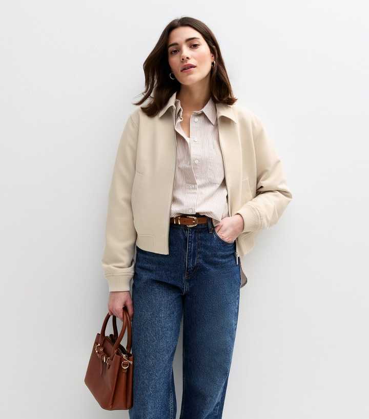 Cream regular-length bomber jacket worn with high-rise blue jeans, showing the hem sitting around the upper hip